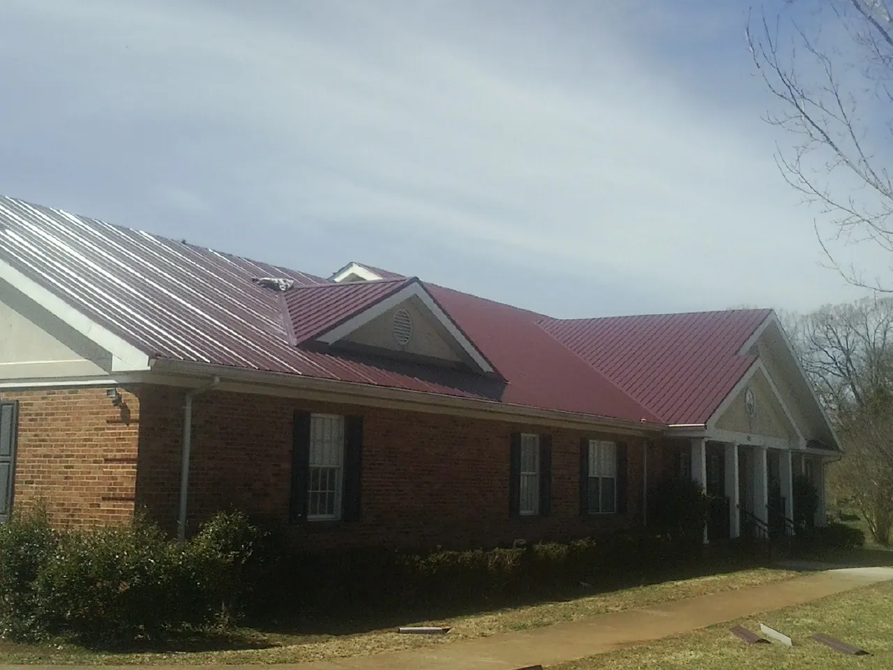 Red metal roof with gabled entries on a long brick building, from a Hail Damage Roof Repair job in Accident
